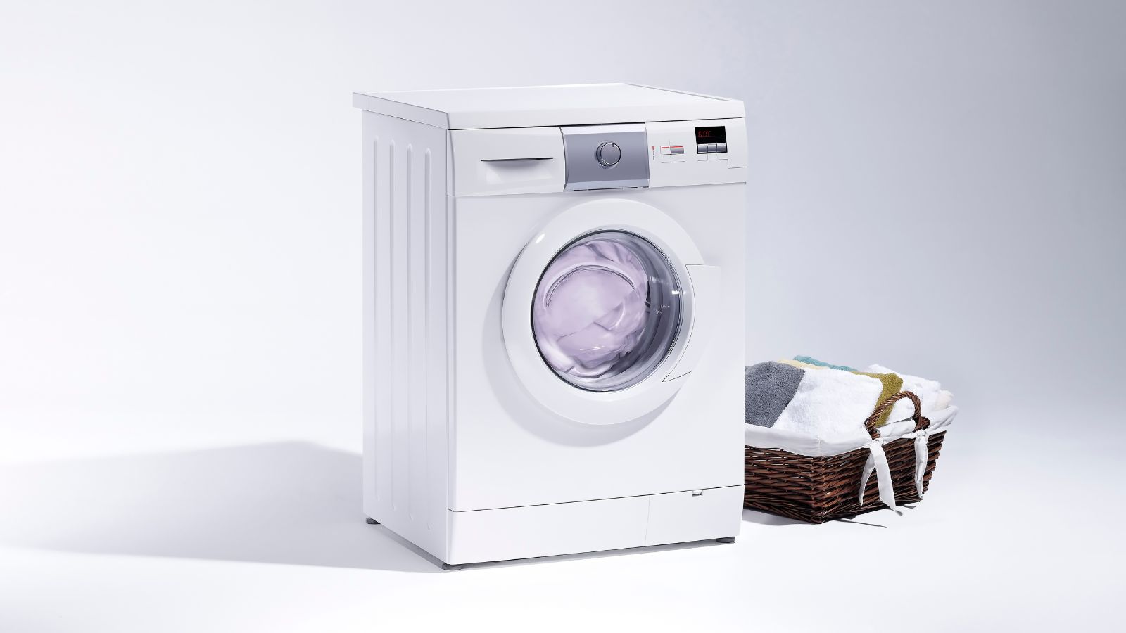 A white washing machine and a basket of laundry isolated on a white background