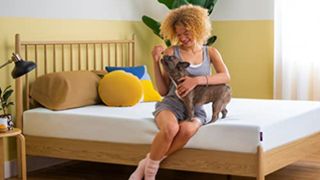 A woman and her dog sit on top of the Purple NewDay mattress
