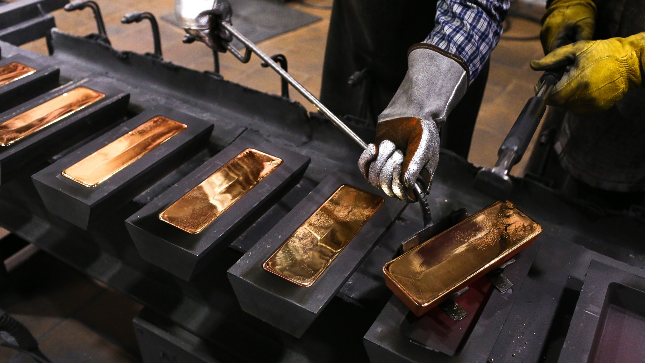 Two goldsmiths extracts gold bars from metal molds.