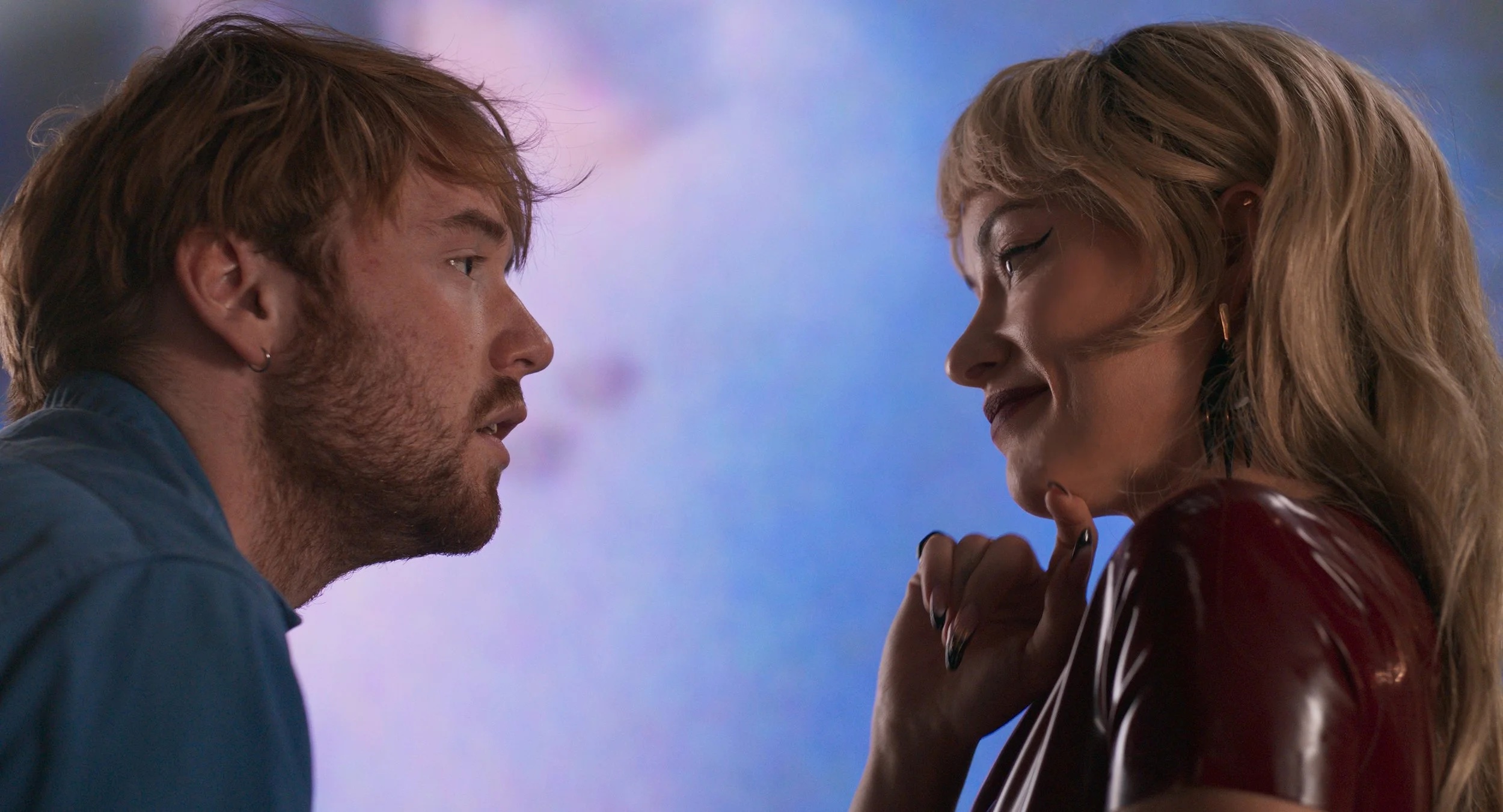 cooper hoffman as elliot leaning in to talk to olivia wilde as erika tracy as she wears all red latex in the movie i want your sex