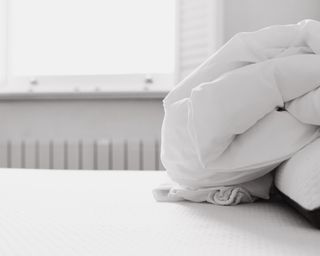 Clean white mattress with scrunched white duvet on top in front of window