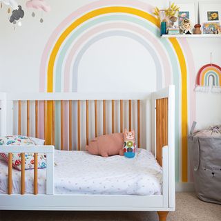 girls nursery with rainbow painted wall mural and cot