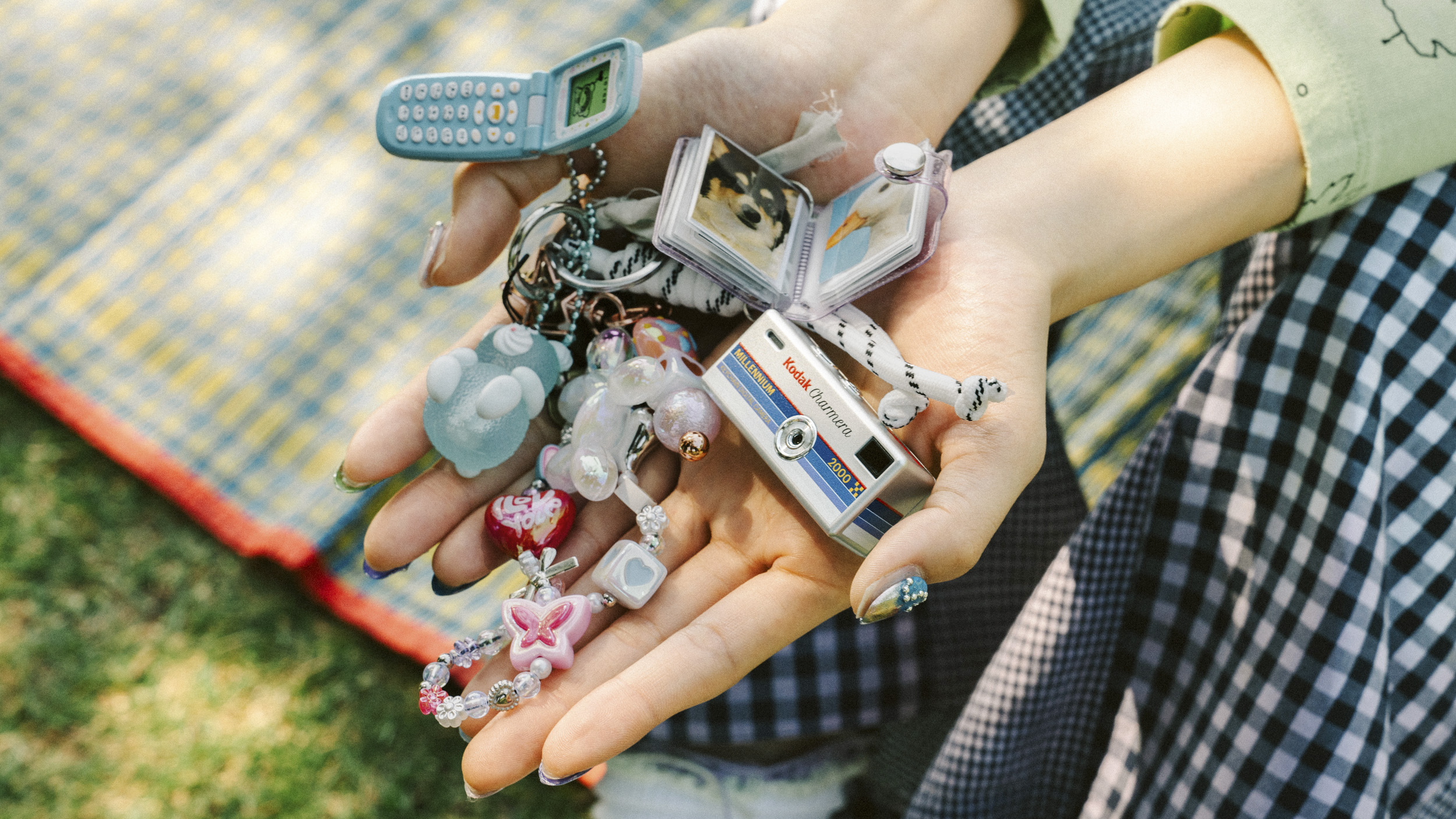 A Kodak Charmera Millennium Edition camera in person's hands, alongside other Y2K-inspired trinkets