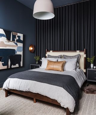 color drenched bedroom in dark navy blue with a dark wooden bedrom and neutral bedding with woven carpet