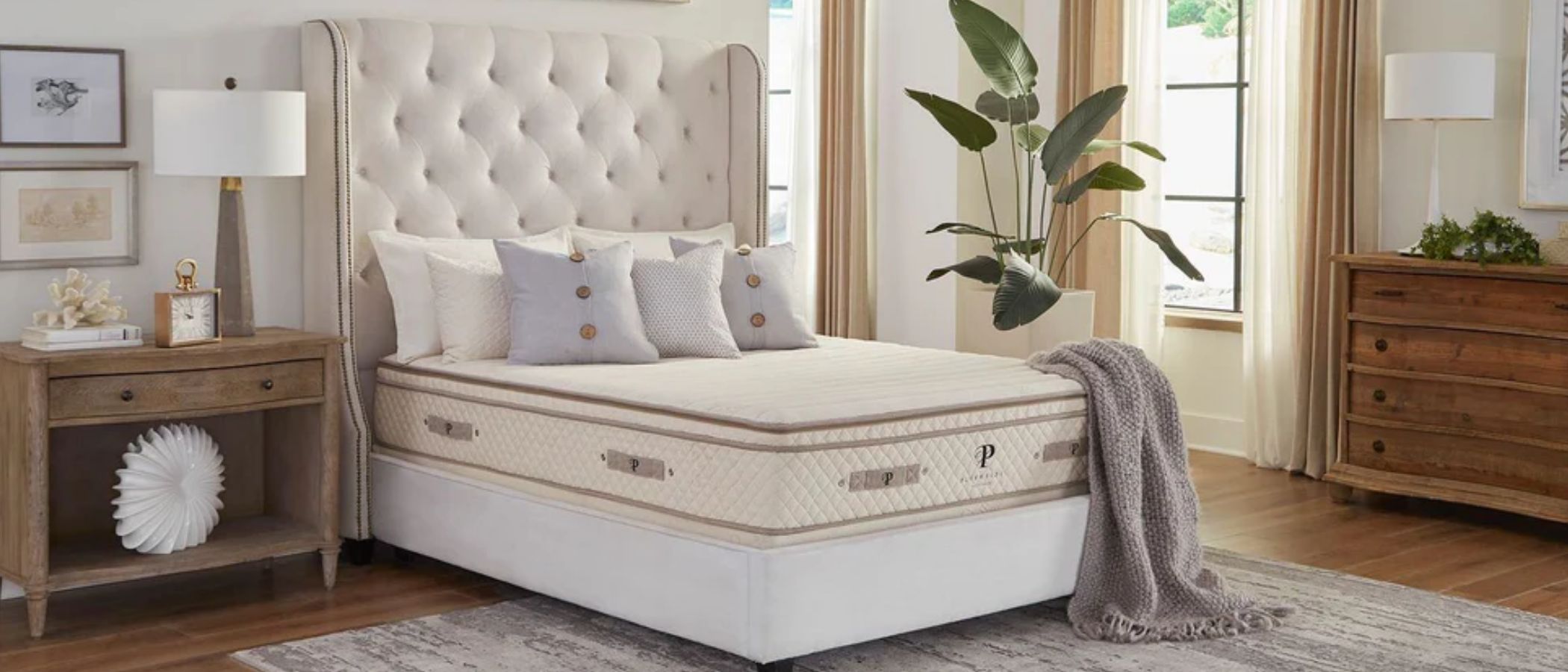 The image shows the PlushBeds Botanical Bliss Organic Latex Mattress on a white bedframe in a neutral bedroom