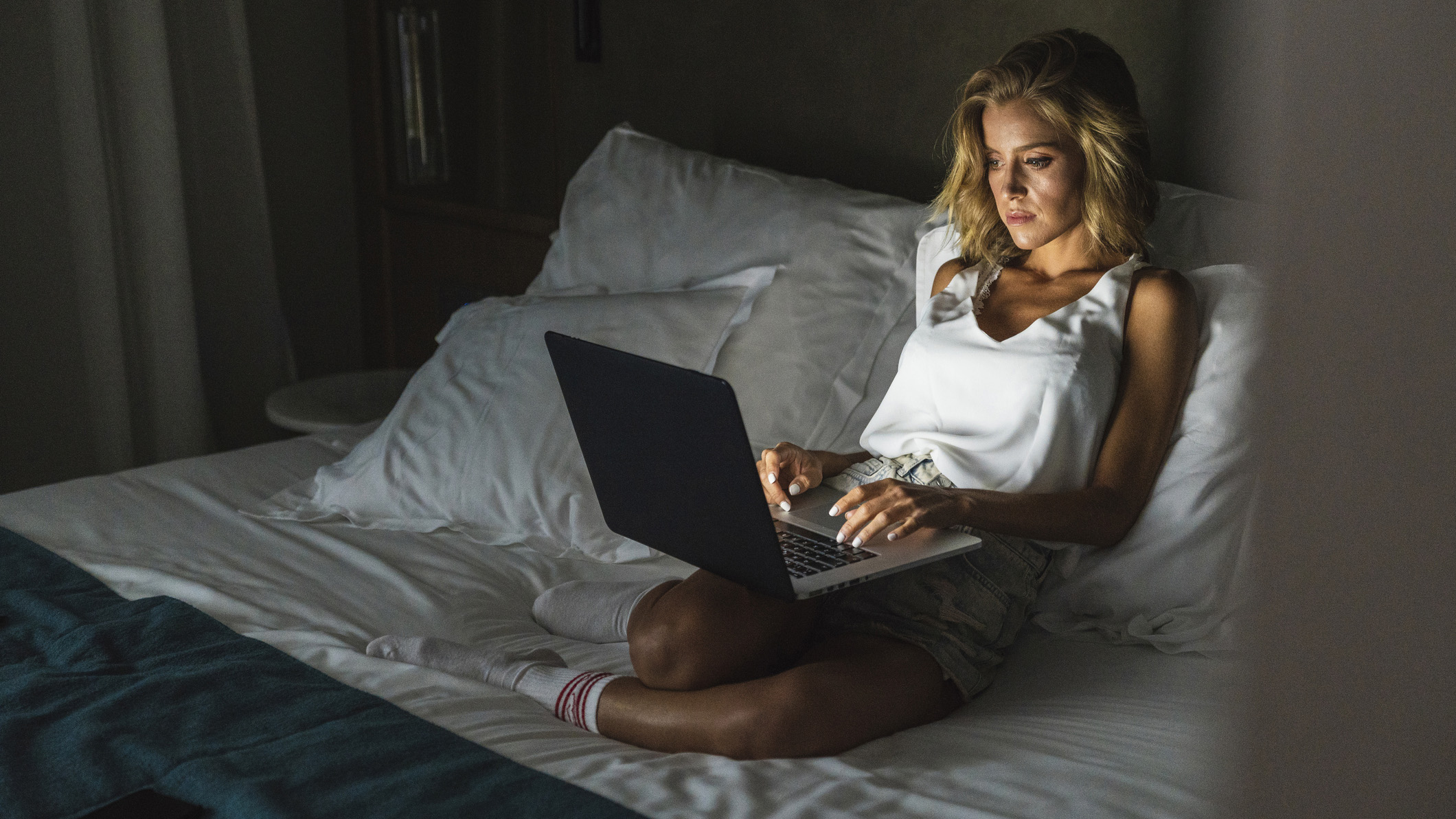 Blonde haired woman working on laptop in bed close to bedtime