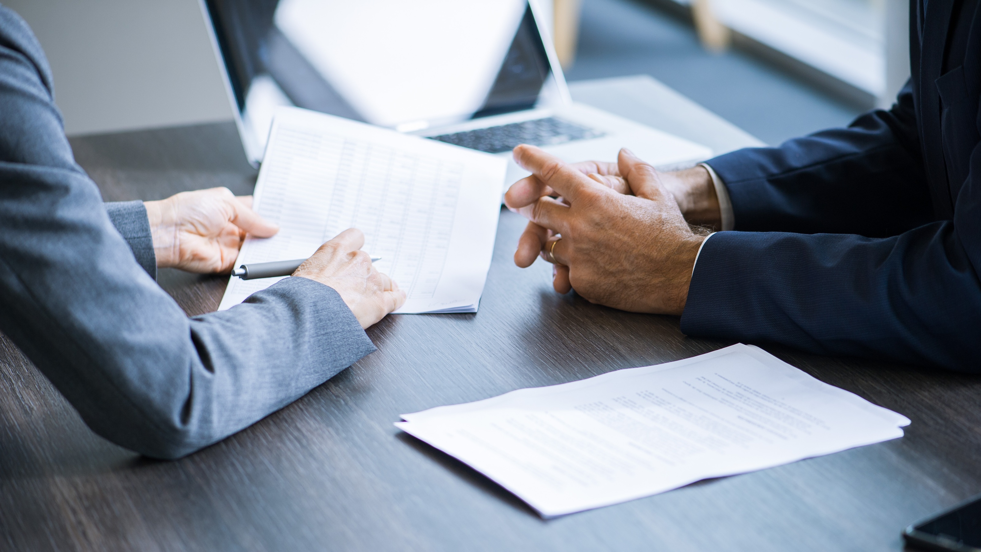 An adviser and a client work together at a desk with paperwork, only their hands and forearms showing.