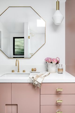 pink and white bathroom with pink vanity, gold fixtures and fittings
