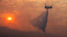A helicopter drops water on a wildfire in California in 2024.