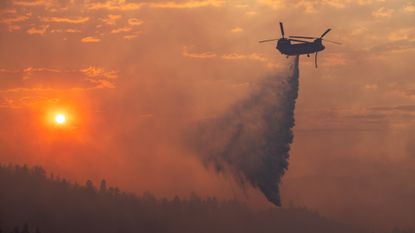 A helicopter drops water on a wildfire in California in 2024.