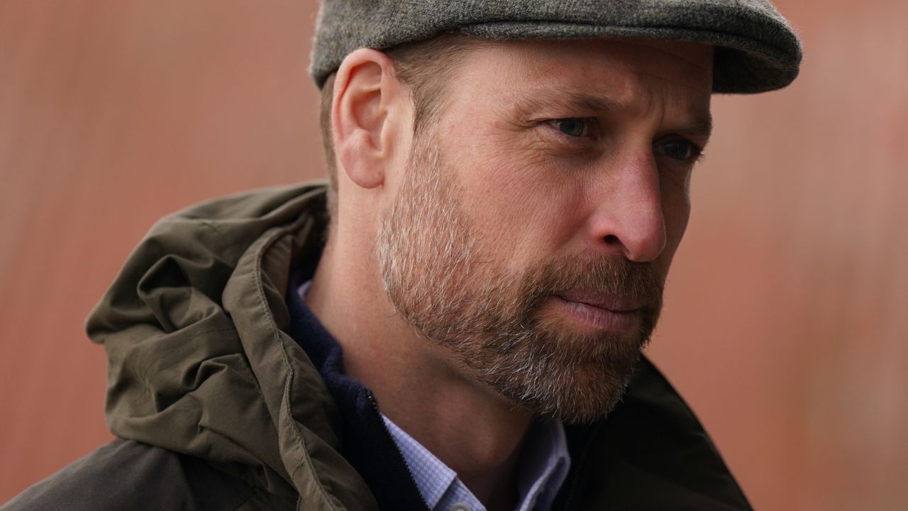 Prince William wearing a green coat with a hood and a gray flat cap 