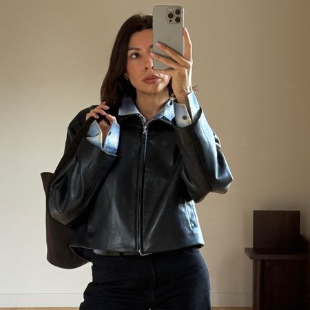 A woman wears a blue flannel shirt, leahther jacket, and black jeans.