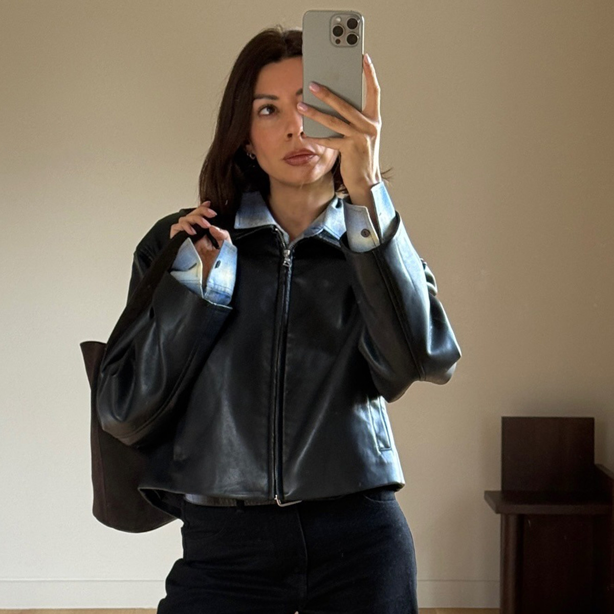 A woman wears a blue flannel shirt, leahther jacket, and black jeans.