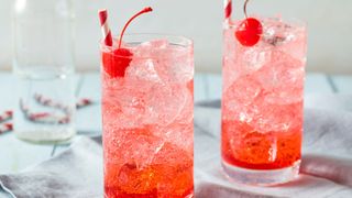 Shirley Temple cocktail with ice and maraschino cherry sitting in tall glass