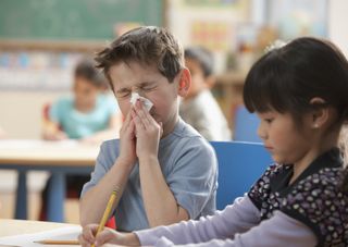 A boy sneezing into a tissue in a classroom
