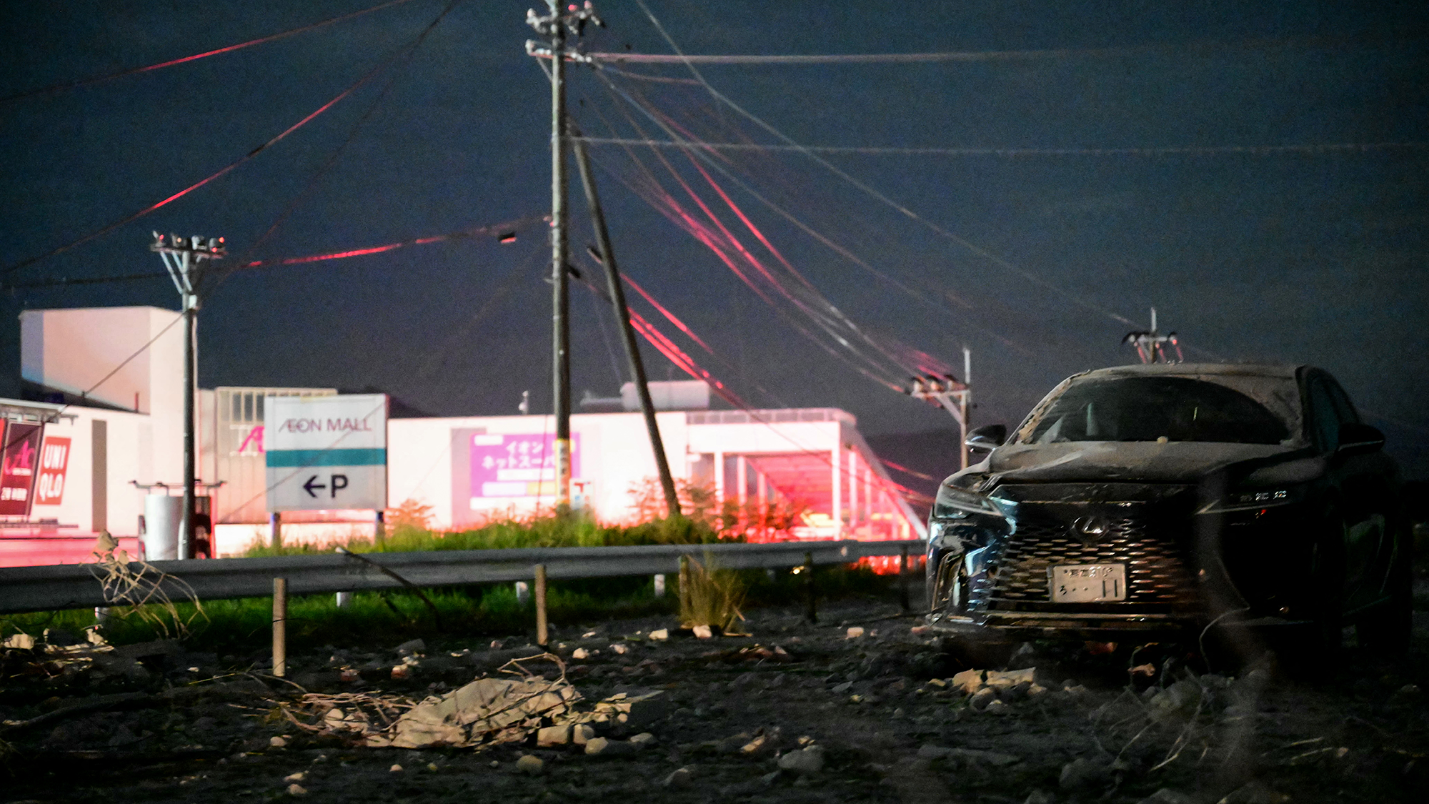 A car sits next to a broken road with buildings behind it
