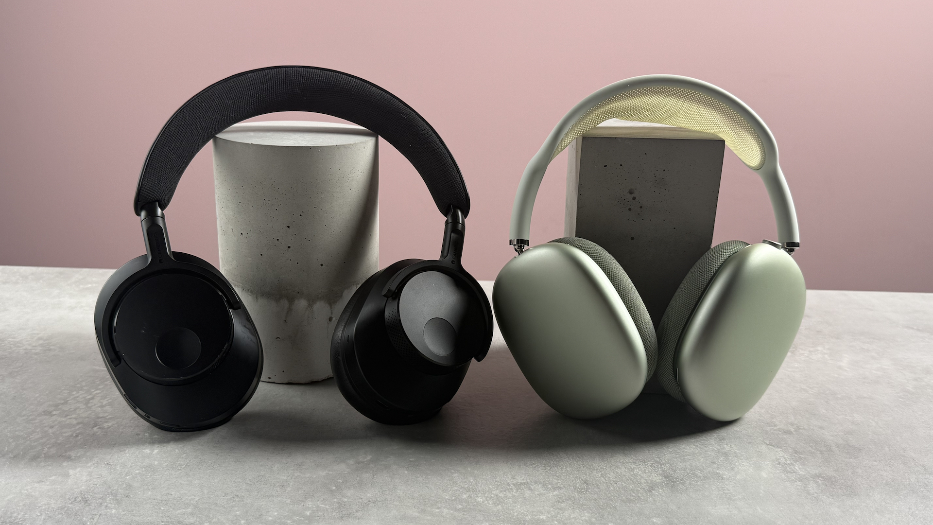 The Cambridge Audio Melomania P100 and AirPods Max propped up in front of a pink background.