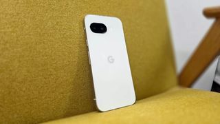 Google's Pixel 9a in the Porcelain color option leaning against a mustard armchair