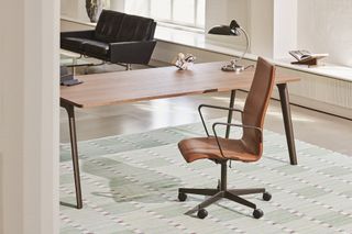A brown leather office chair with a high back. It's photographed set next to a wooden work desk.