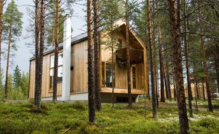 An outdoor house located in a forest made of timber. The front has a balcony.