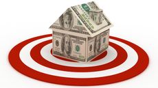 A home constructed of hundred-dollar bills sits in the center of a target.