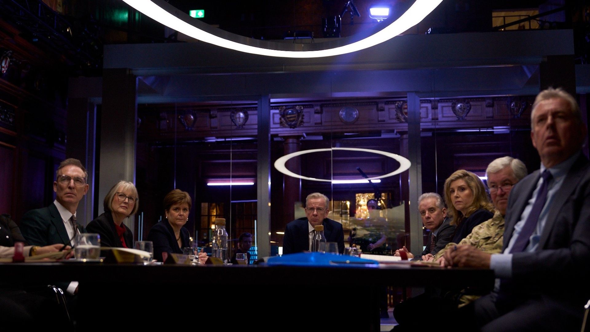 A fake government cabinet sits around a boardroom table