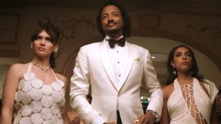 Koumba dressed in white tux with beautiful women by his side in Pluribus Episode 6