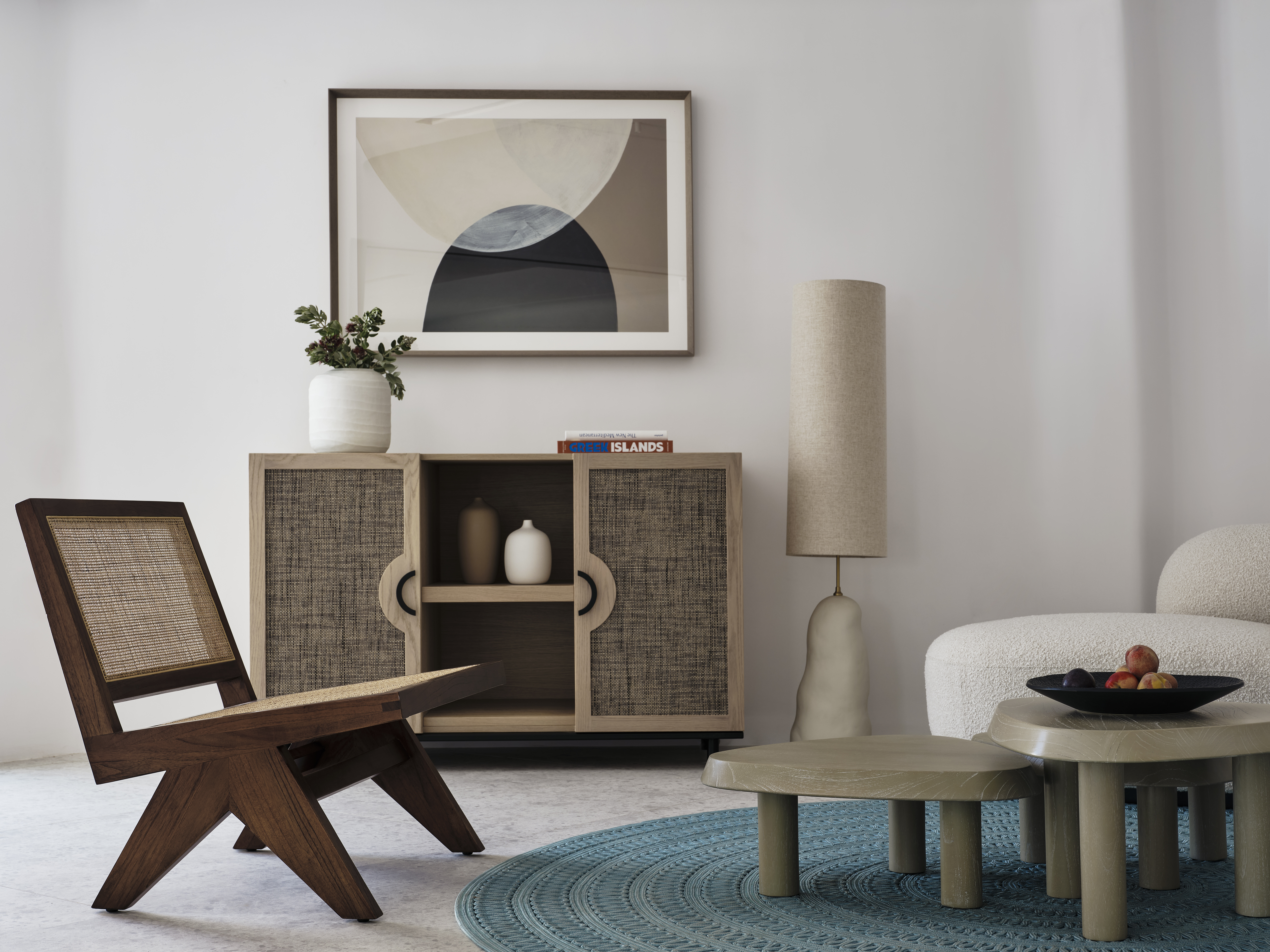 A contemporary hotel room&#039;s decor punctuated by beige and wood furnishings, a sea blue tufted rug, ceramic floor lamps, and framed artwork.