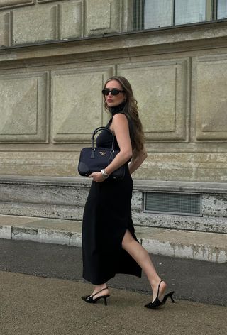 a black maxi skirt outfit showcasing a woman wearing black sunglasses with a gray sleeveless turtleneck, black maxi skirt, black prada bag, silver watch, and black slingback heels