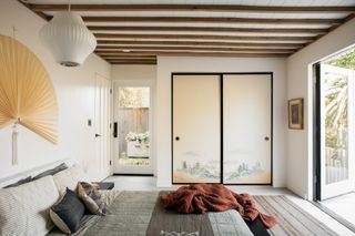 japandi style bedroom with japanese fan styled over the bed, painted cabinet doors, wood panelled ceiling, and earthy tones on the bed