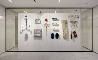 A large glass display case with various items of clothing mounted on a white wall with a grid pattern of small holes in it.