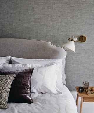 Relaxing and stylish bedroom with grey textured wallpaper, white and brown bedding. A double bed and angled wall light.