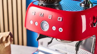 a red smeg espresso machine with burr grinder is photographed against a blue background