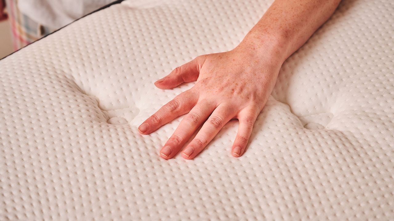 A close up of a hand on the surface of the Plank Firm mattress (Firm side.) The hand is pushing into a bed but not making much of an impression on the materials