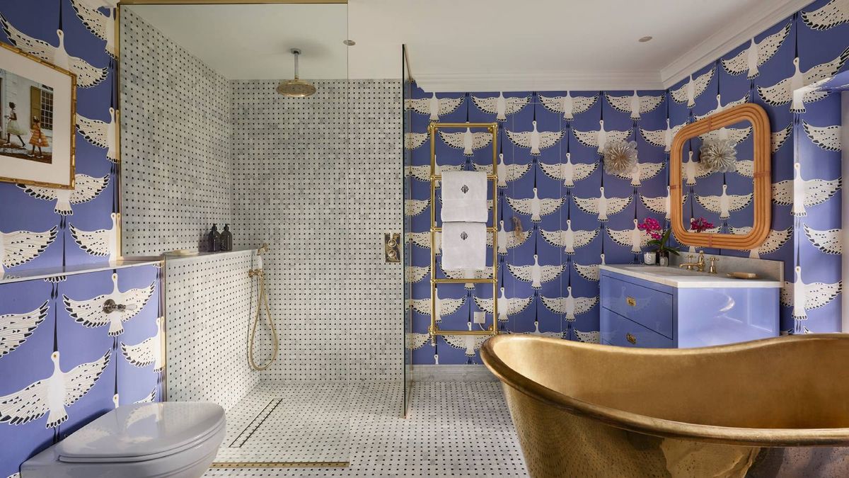 bathroom with blue wallpaper with large white birds, mosaic tiled shower enclosure, large copper bath, sink and vanity unit and gold towel rail