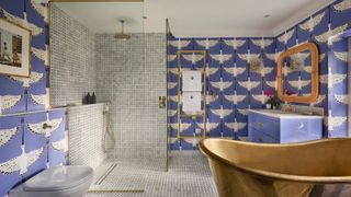 bathroom with blue wallpaper with large white birds, mosaic tiled shower enclosure, large copper bath, sink and vanity unit and gold towel rail