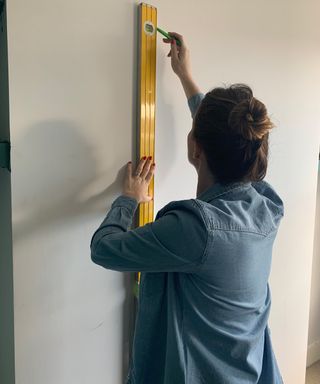 Kate Sandhu using yellow builder's ruler on wall to measure for door frame