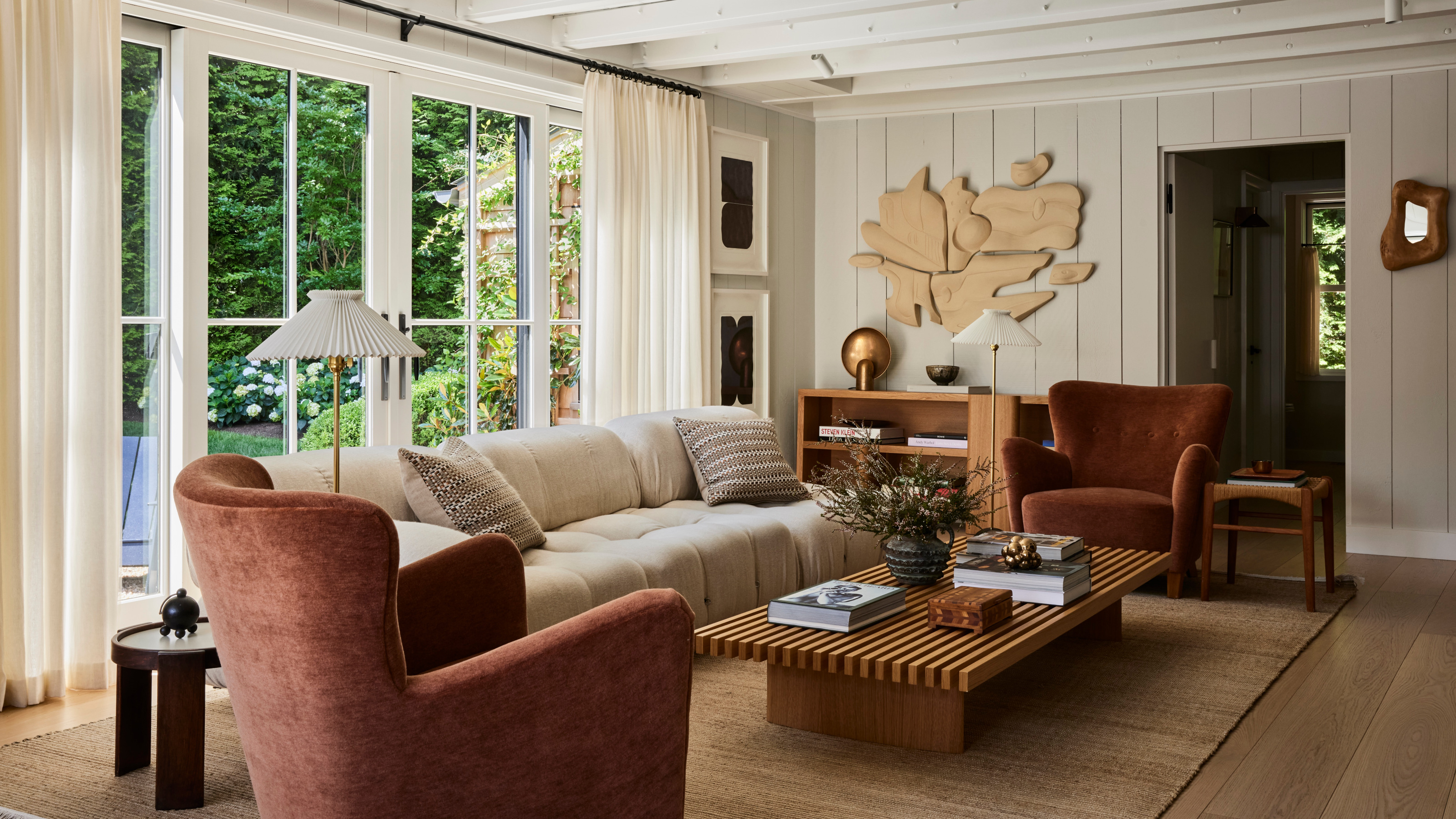 Living room with white panelled walls, wood floor, rust armchairs, cream sofa, striped marquetry coffee table