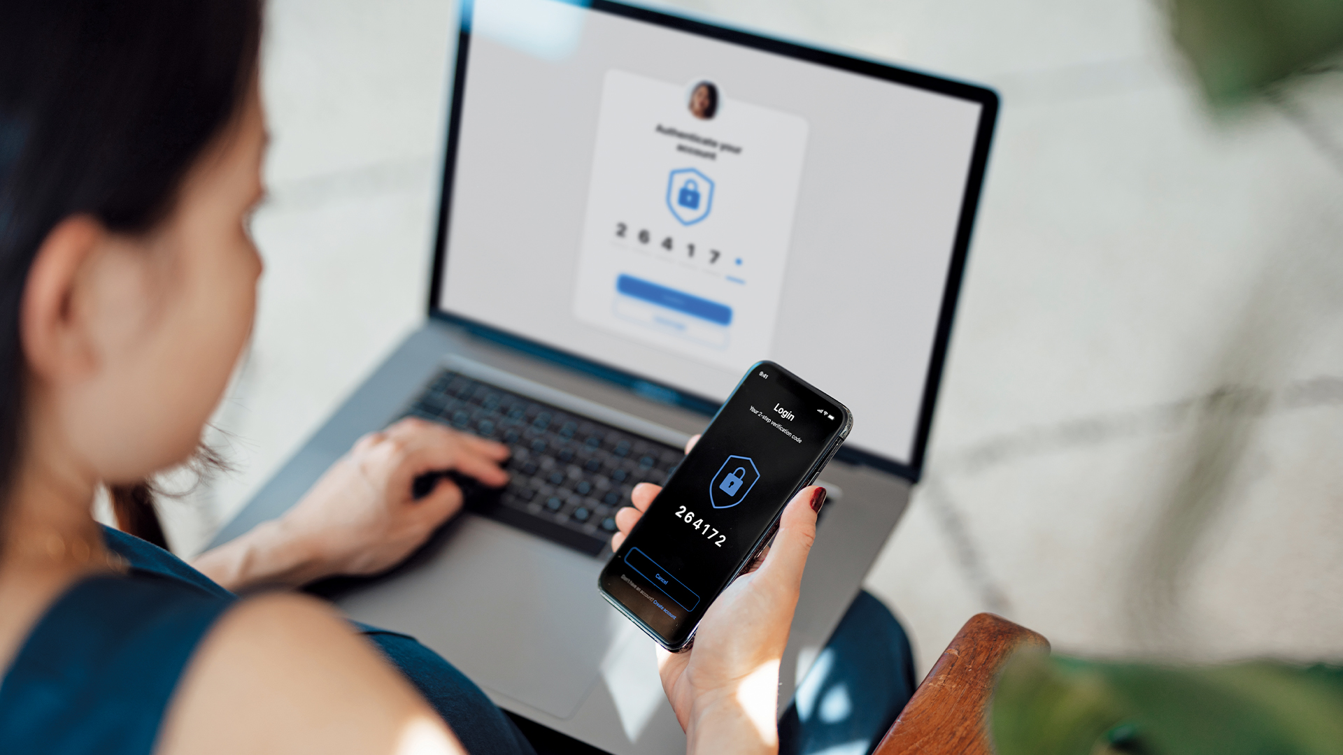 A woman logs onto something on her laptop using two factor authentication codes from her phone