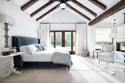 bedroom with white shiplap walls and blue bedhead stone floors and picture windows