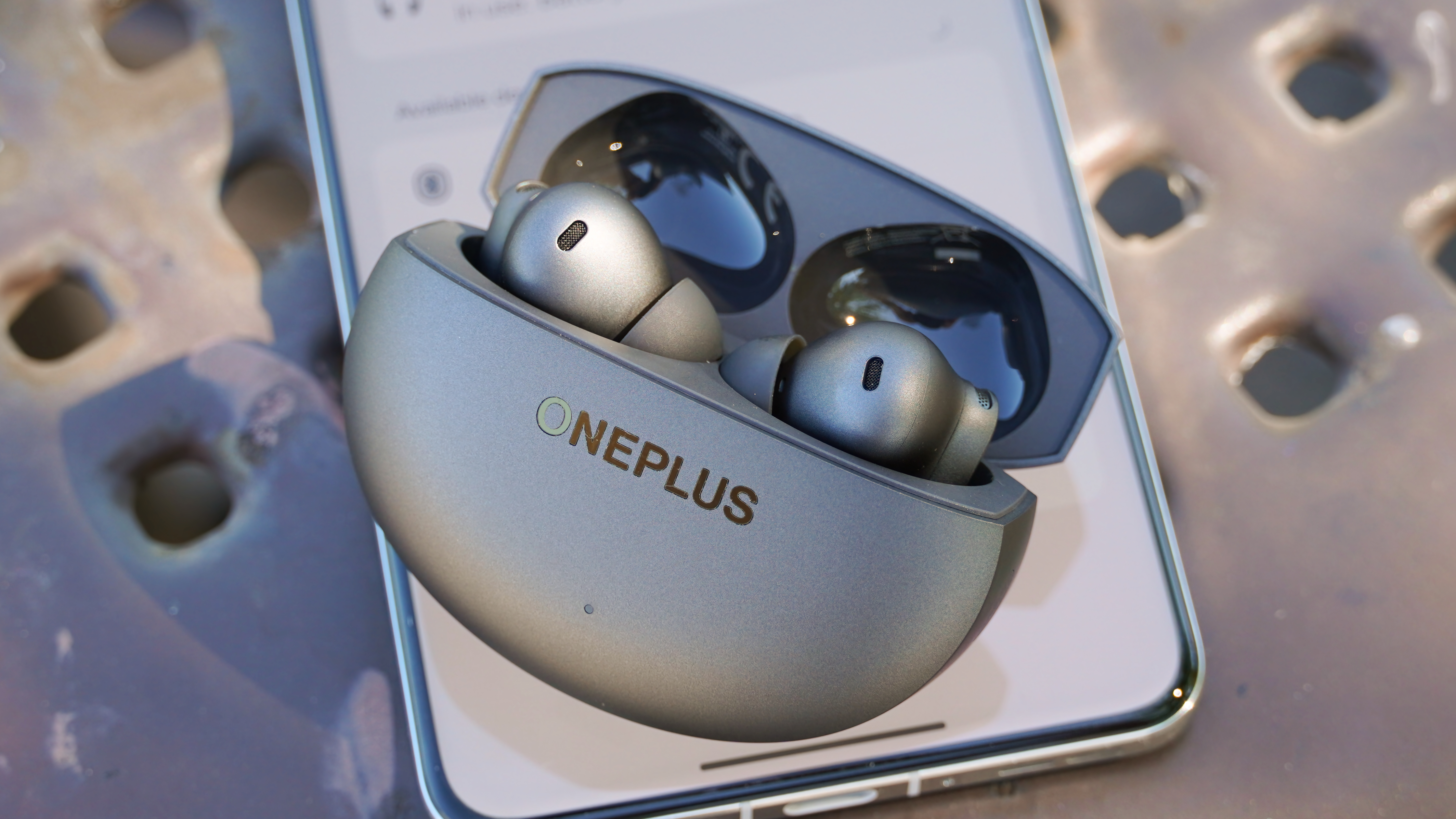 The OnePlus Buds 4 in Storm Gray sitting atop a OnePlus 13.
