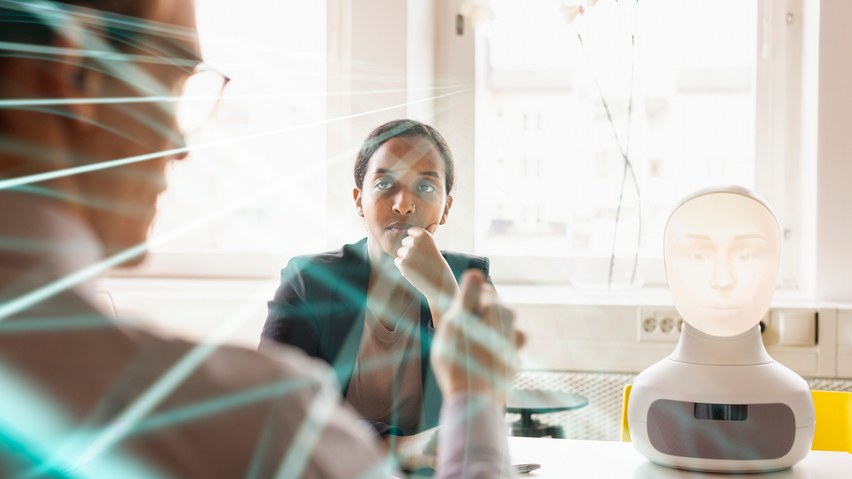 A woman looks at a man in a board room, with a bust of an android on the table while beams of light stream towards the camera