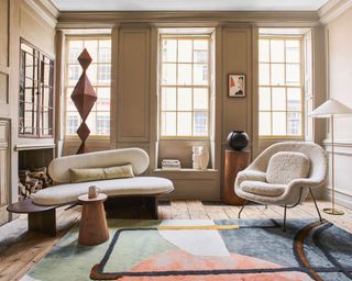 Living room with wooden floor and panelled walls, three large sash windows with wooden shutters, sculptural vases and items on display.