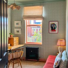 Home office with striped wallpaper, black radiator, wooden desk and striped blind on window