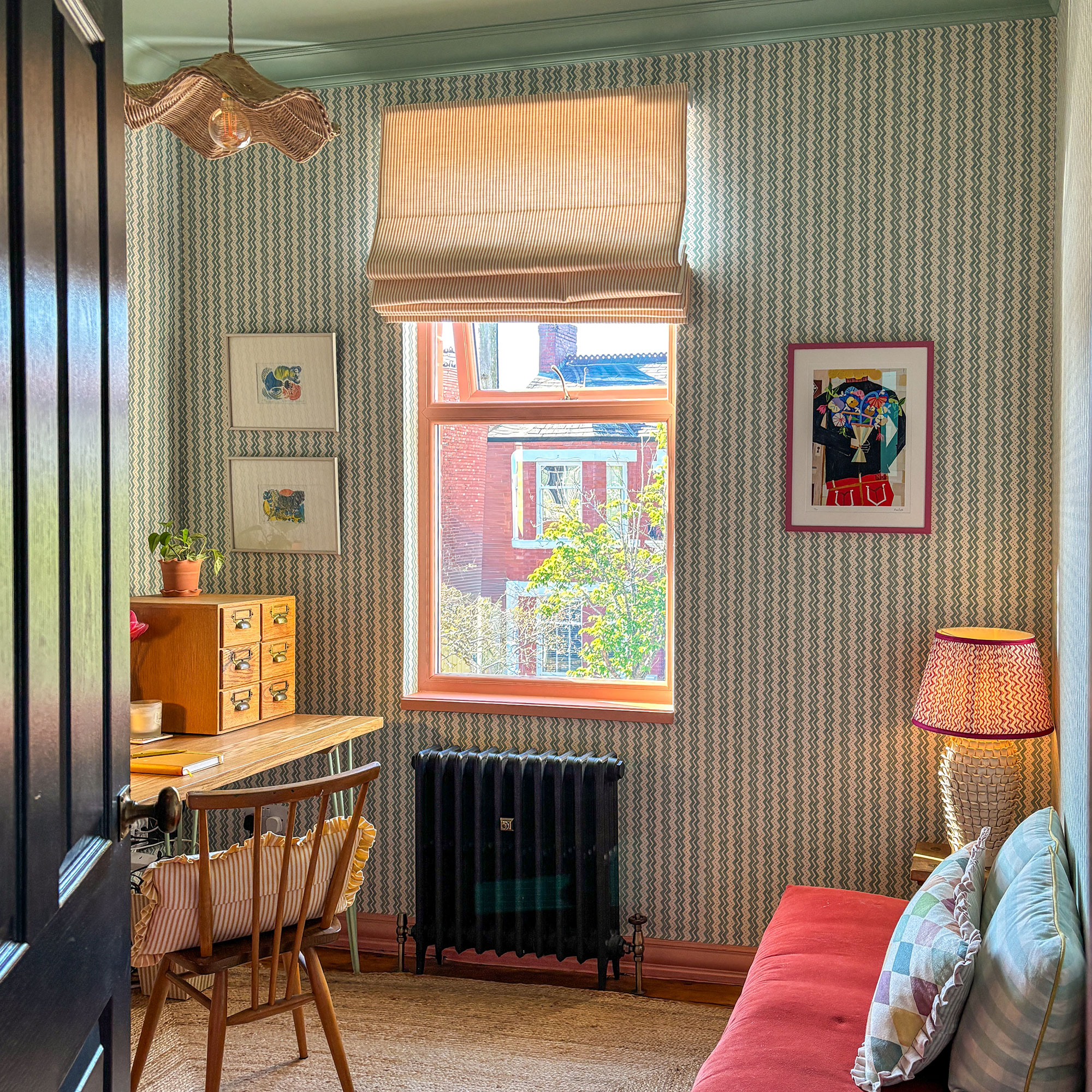 Home office with striped wallpaper, black radiator, wooden desk and striped blind on window