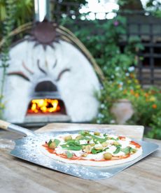 An olive and basil pizza ready to be loaded into a pizza oven