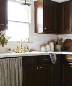 A dark wood kitchen with marble countertops, traditional decor, and a striped cabinet skirt under the sink