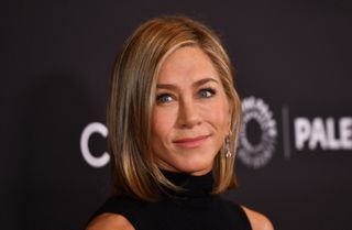 Image of Jennifer Aniston with a blonde side part bob, wearing a black high-neck dress