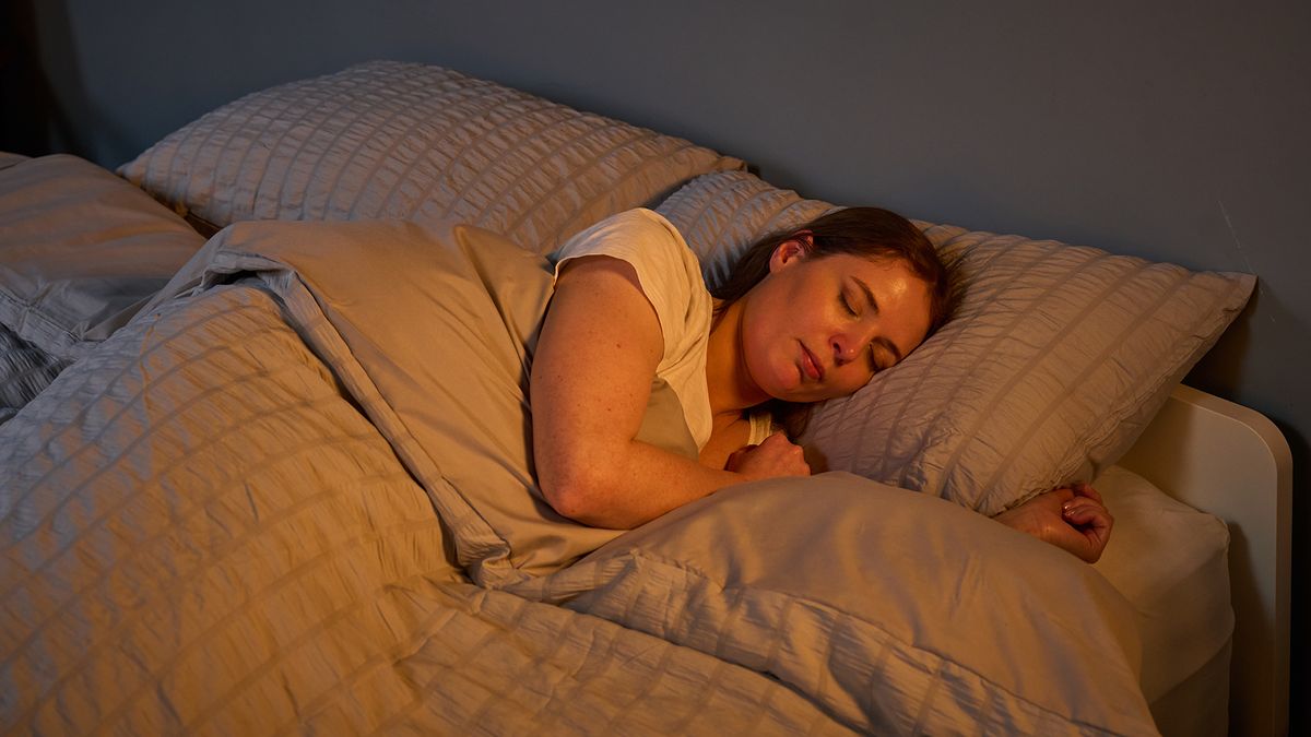 Tom's Guide mattress tester Ruth Jones, dressed in a white bed top, sleeps on her side on the Helix Midnight Luxe mattress in our Mattress Testing Lab