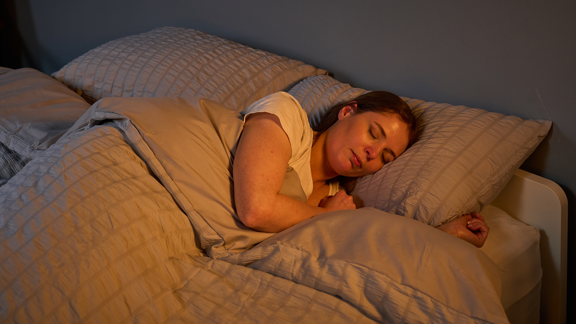 Tom's Guide mattress tester Ruth Jones, dressed in a white bed top, sleeps on her side on the Helix Midnight Luxe mattress in our Mattress Testing Lab